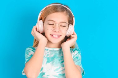 Memnun küçük beyaz kız hoş melodiler dinlemeyi seviyor. Müzik seti kulaklıklarını takıyor, gözlerini kapatıyor. Müzikle boş zaman geçirmek