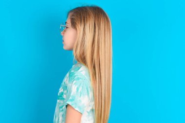 Mavi arka planda modaya uygun tişörtler giyen beyaz bir kızın profil portresi. Boş dişli bir gülümseme.