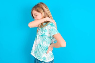 Mavi arka planda modaya uygun tişört giyen beyaz kız sırt ağrısı çekiyor.