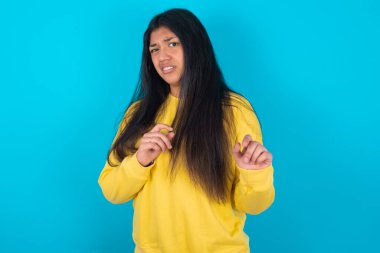 Ne kadar iğrenç! Mavi arka planda sarı kazak giyen hoşnutsuz Latin kadın iğrenç bir yüz ifadesi sergiliyor..