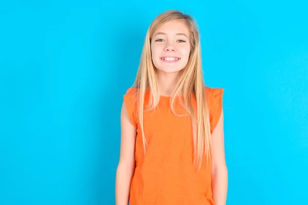 小女孩穿着橙色的T恤 背景是蓝色的 脸上挂着灿烂的微笑 脸上带着愉快的表情 积极情绪概念 — 图库照片
