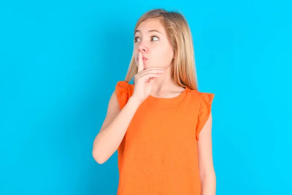 Malá Holčička Oranžovém Tričku Modrém Pozadí Mlčení Gesto Udržuje Ukazováček — Stock fotografie