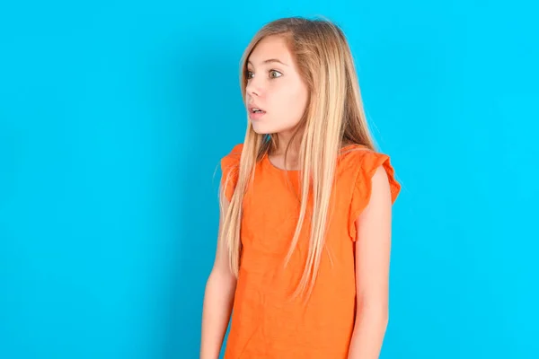 Niña Pequeña Vistiendo Camiseta Naranja Sobre Fondo Azul Mira Lado —  Fotos de Stock