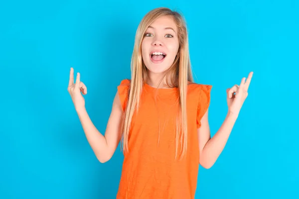 Kleines Mädchen Mit Orangefarbenem Shirt Vor Blauem Hintergrund Lässt Rock — Stockfoto