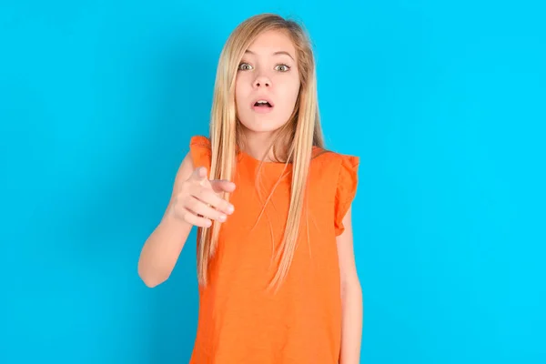 Schockiertes Kleines Mädchen Orangefarbenem Shirt Vor Blauem Hintergrund Zeigt Mit — Stockfoto