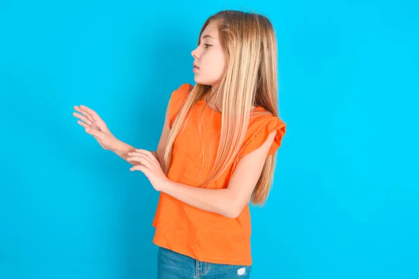 Niezadowolony Dziewczynka Nosi Pomarańczowy Shirt Niebieskim Tle Trzyma Ręce Kierunku — Zdjęcie stockowe