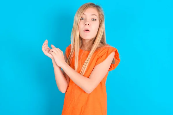 Zaskoczony Emocjonalny Dziewczynka Nosi Pomarańczowy Shirt Niebieskim Tle Masuje Dłonie — Zdjęcie stockowe