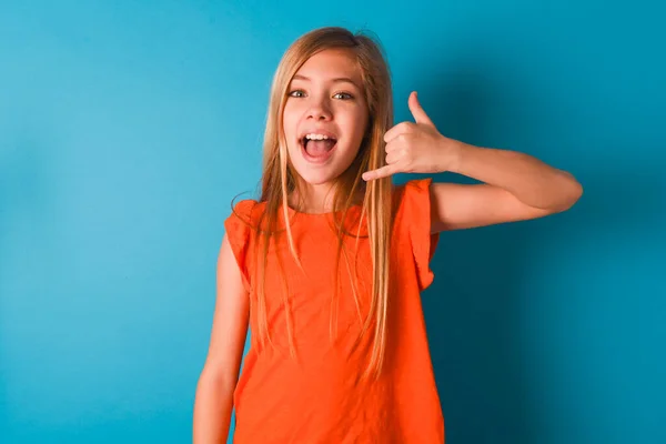 Klein Meisje Draagt Oranje Shirt Blauwe Achtergrond Maakt Telefoon Gebaar — Stockfoto