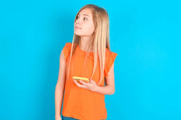 Liten Flicka Bär Orange Shirt Över Blå Bakgrund Håller Mobiltelefon — Stockfoto