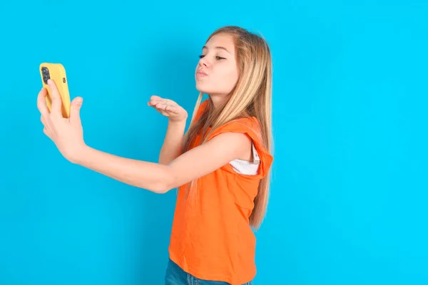 Meisje Draagt Oranje Shirt Blauwe Achtergrond Blaast Lucht Kus Camera — Stockfoto