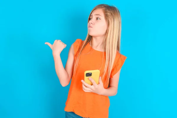 Kleines Mädchen Mit Orangefarbenem Shirt Über Blauem Hintergrund Zeigt Daumen — Stockfoto