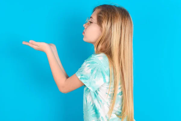 プロフィールサイドビュー エアキスを送信する青い背景の上にトレンディなTシャツを着ている魅力的な小さな白人少女の肖像画 — ストック写真