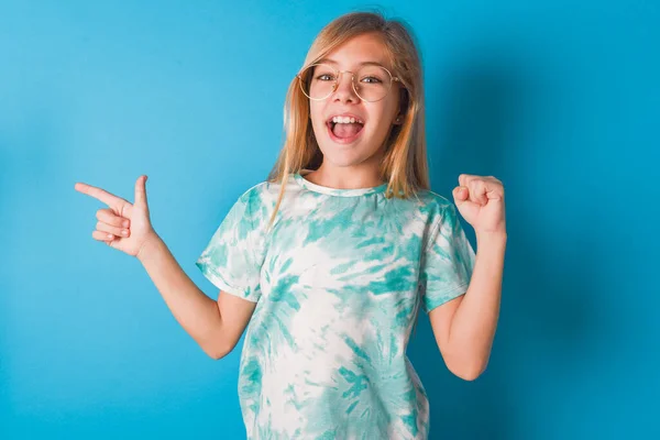 年轻的高加索女孩 穿着时髦的T恤 带着蓝色背景点站在空旷的空间里 举起拳头 摆出一副胜利者的架势 — 图库照片