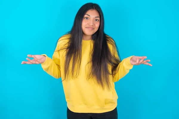 Puzzled Clueless Latin Woman Wearing Yellow Sweatshirt Blue Background Arms — Stock Photo, Image