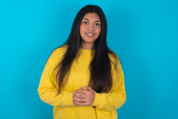 ビジネスコンセプト 自信を持って顔を握る青い背景の上に黄色いスウェットシャツを着たラテン系女性の肖像画 — ストック写真