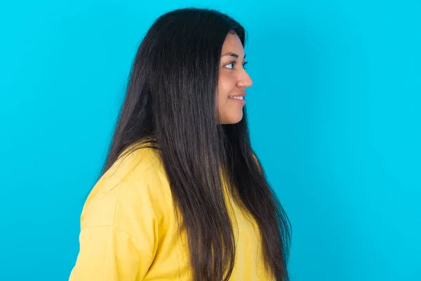 健康な肌で青い背景に黄色いスウェットシャツを着て笑顔のラテン系女性のプロフィールは 屋外散歩をする準備ができて熟考的な表現を持っています — ストック写真