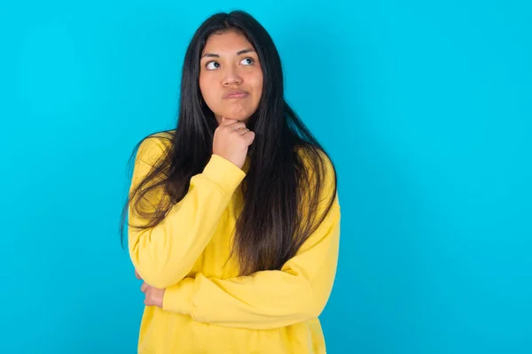 woman  with hand under chin and looking sideways with doubtful and skeptical expression, suspect and doubt.