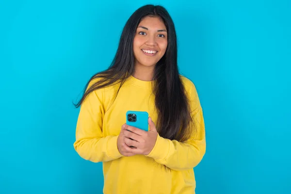 Mujer Latina Sonriente Con Sudadera Amarilla Sobre Fondo Azul Amigable —  Fotos de Stock