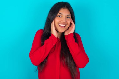  Mavi arka planda kırmızı tişört giyen Latin kadın neşeli ve neşeli görünüyor.