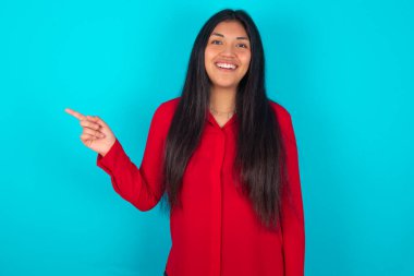   Mavi arka planda kırmızı t-shirt giyen Latin bir kadın mutlu bir şekilde boş alana gülüyor. İyi haber ya da beklenmedik satıştan etkilenen, indirimli alışveriş teklifini gösteriyor..