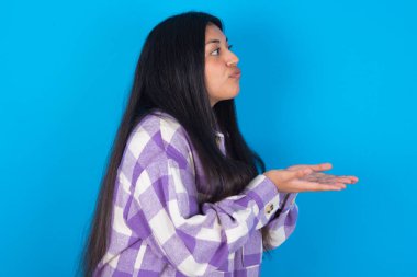 Profil yan görünümü portresi. Mavi arka planda ekose gömlek giyen çekici Latin kadın hava öpücüğü gönderiyor.