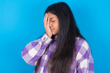  Mavi arka planda ekose gömlek giyen Latin bir kadın. Ağlarken suratını ellerle kapatan üzgün bir ifade. Depresyon kavramı.