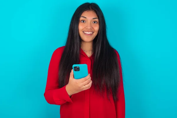 Mujer Latina Vistiendo Camiseta Roja Sobre Fondo Azul Sostiene Teléfono —  Fotos de Stock