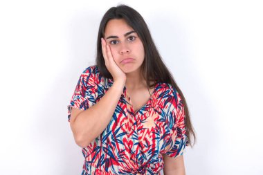 Beyaz duvarın üzerinden renkli elbiseler giyen üzgün, yalnız, güzel esmer kadın yanağına dokunuyor alt dudağını ısırıyor ve hoşnutsuzca bakıyor. Kötü duygular