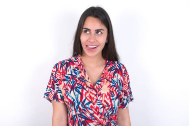 Beyaz duvarın üzerinden renkli elbiseler giyen komik, genç, güzel esmer kadın yüzünü buruşturup, haç çıkartıyor..