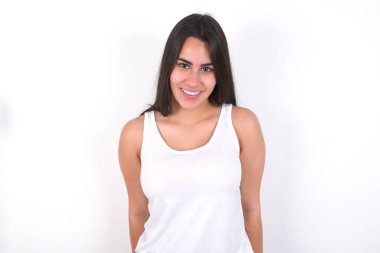 Beyaz duvarda beyaz bluz giyen esmer bir kadın. Hoş, ışıltılı bir gülümsemesi var. Pozitif duygu kavramı