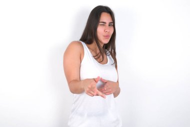 Hey sen, bang. Neşeli ve karizmatik güzel esmer kadın beyaz bluz giyiyor beyaz göz kırpıyor ve parmaklarıyla kameraya doğru bakıyor mutlu ve arsız..