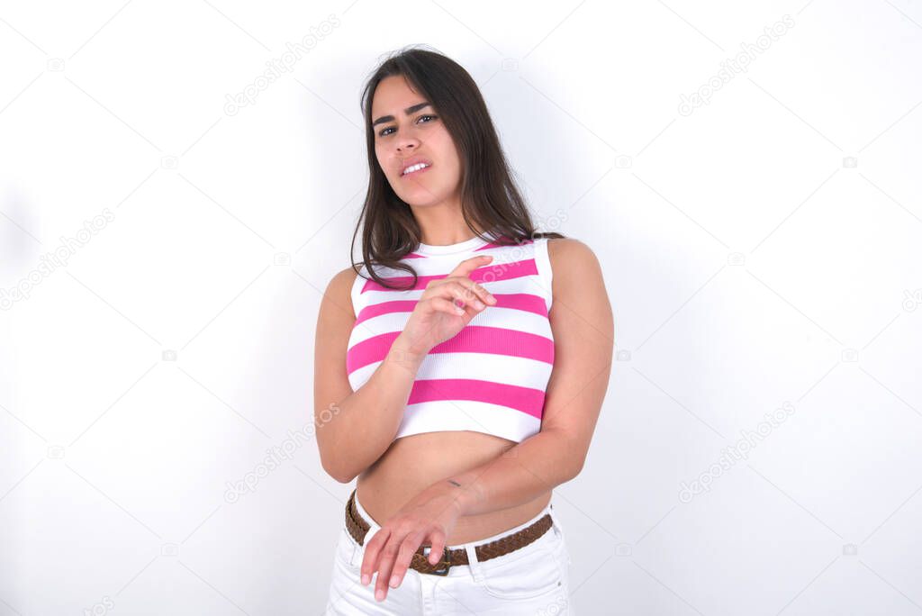 Ugh how disgusting! Displeased beautiful brunette woman wearing striped crop top over white wall, has dissatisfied facial expression as sees something abominable.