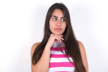 Hayalperest esmer kadın beyaz duvarın üzerinde çizgili bir bluz giyiyor, hoş bir ifade takınıyor, yan bakıyor, elini çenesinin altında tutuyor, hoş bir şeyler düşünüyor..