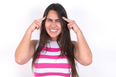 Esmer kadın beyaz duvarın üzerinde çizgili bluz giyiyor. Ciddi bir bakışla bir fikir üzerinde yoğunlaşıyor. Her iki işaret parmağı da alnını işaret ediyor..