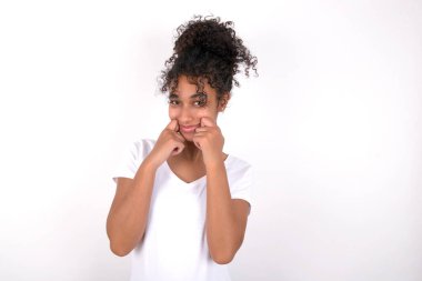 Afro saçlı, beyaz önlüklü, beyaz tişörtlü, gözleri kapalı güzel bir kız ellerini yanaklarından ayırmıyor ve gülümsüyor. Hoş bir şey hayal ediyor.