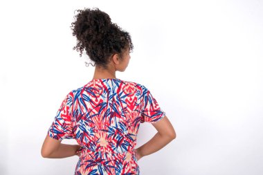 Beyaz duvarın üzerinde renkli elbiseler giyen güzel melez bir kadının arka görüntüsü. Stüdyo Çekimi.