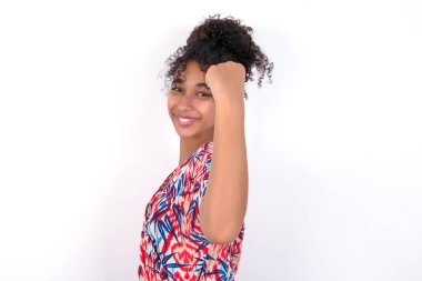 Neşeli kız iyi haberler almaktan, yumruğunu sıkmaktan ve kazanan jestler yapmaktan memnun. Beyaz duvarda renkli elbiseler giyen güzel melez bir kadın.