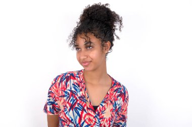 Sakin kız yukarı bakıyor. Beyaz duvarda renkli elbiseler giyen güzel melez bir kadın.