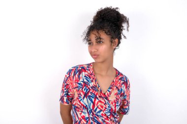 Şaşırmış bir kız, kıvrımlı dudaklar ve endişeli bir bakış, önünde korkunç bir şey görüyor. Beyaz duvarda renkli elbiseler giyen güzel melez bir kadın.