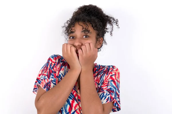 Tırnaklarını yiyen endişeli bir kız. Beyaz duvarda renkli elbiseler giyen güzel melez bir kadın.