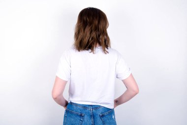 Bir kızın arka görünüşü. Stüdyo çekimi. Beyaz arka planda beyaz tişört giyen beyaz bir kadın. 