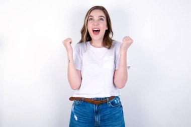 Kız heyecanla bakıyor, ellerini havada tutuyor, beklenmedik bir şey fark ediyor. Beyaz arka planda beyaz tişört giyen beyaz bir kadın. 