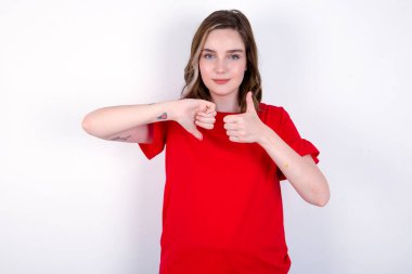 Beyaz arka planda kırmızı tişört giyen beyaz kadın baş parmağını aşağı işareti ile gösteriyor.