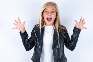 Beyaz arka planda motosiklet ceketi ve gözlük takan güzel, güzel, güzel bir kız çocuğu harika bir sonuç elde ettikten sonra ağzını ve kollarını açar.