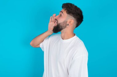 Beyaz tişörtlü beyaz sakallı beyaz bir adam mavi arka plan profili üzerinde, mutlu ve heyecanlı görünüyor, bağırıyor ve uzayı kopyalamak için arıyor..