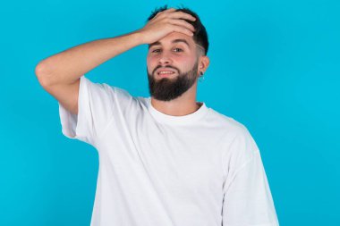 Tüh, ne yaptım ben? Beyaz tişört giyen beyaz sakallı beyaz bir adam mavi arka plan üzerinde korkmuş ve pişmanlık dolu bir ifadeyle el ele tutuşuyor..