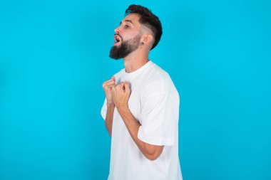 Mavi arka planda beyaz tişört giyen beyaz sakallı beyaz adam zafere ulaştığına seviniyor, yumruklarını sıkıyor, heyecandan gözleri kapalı çığlıklar atıyor, başarılı bir insan..