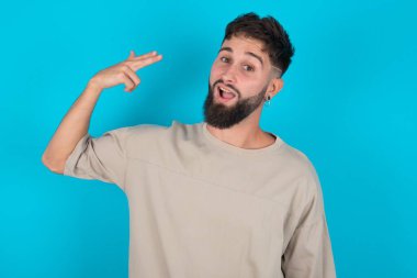 Sakallı, beyaz bir adam mavi arka plan aptalca tişörtler giyip şakaktaki çekimlerde parmaklarıyla intihar jesti yapıyor. Komik manken parmak tabancası yapar.