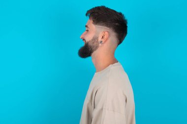 Mavi arka planda günlük tişört giyen hoş sakallı beyaz bir adamın profil portresi boş dişli bir gülümseme gibi görünüyor.