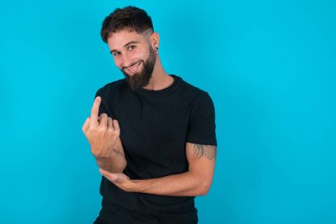 Siyah tişört giyen genç İspanyol sakallı adam mavi arka planda duruyor. Gel buraya, seni selamlıyorum.